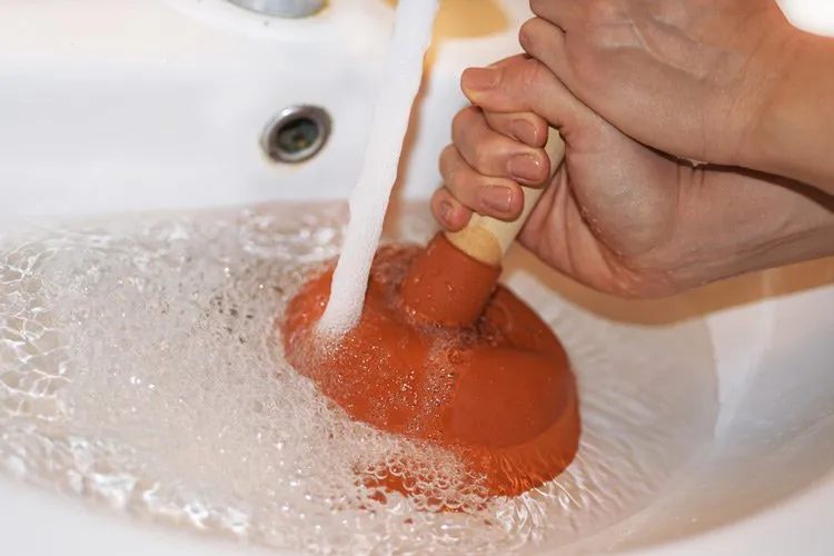 woman using plunger to remove clogged sink 1920w